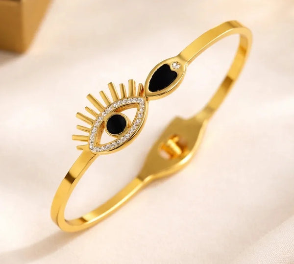Gold plated evil eye bracelet with black enamel and crystal detailing on a white fabric background.