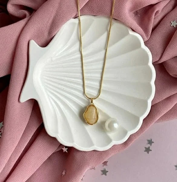 Aesthetic jewellery photography of a gold pendant with textured rim and smooth white center stone.