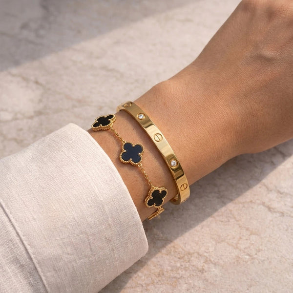 Premium gold plated bracelet stack featuring a black clover chain and crystal studded bangle worn on wrist.