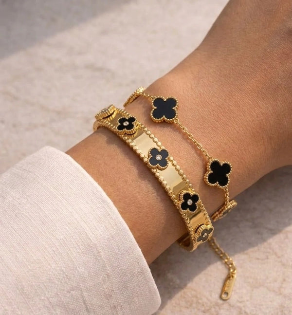 Woman's wrist wearing a stacked anti-tarnish bangle and dainty chain bracelet featuring black clover motifs.