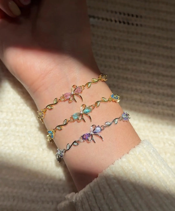 Set of three gold plated bow charm bracelets with pink green and purple crystals.