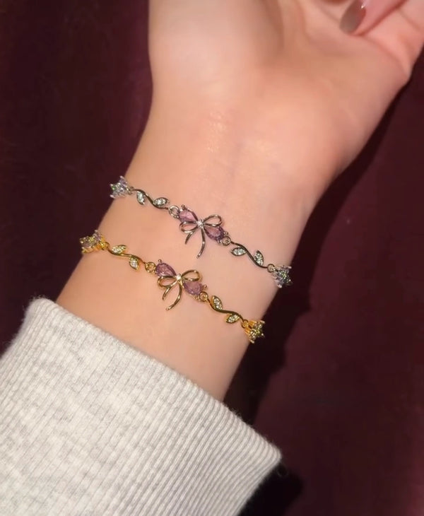 Pair of gold-plated and silver-tone bow bracelets with mauve crystals on a wrist.