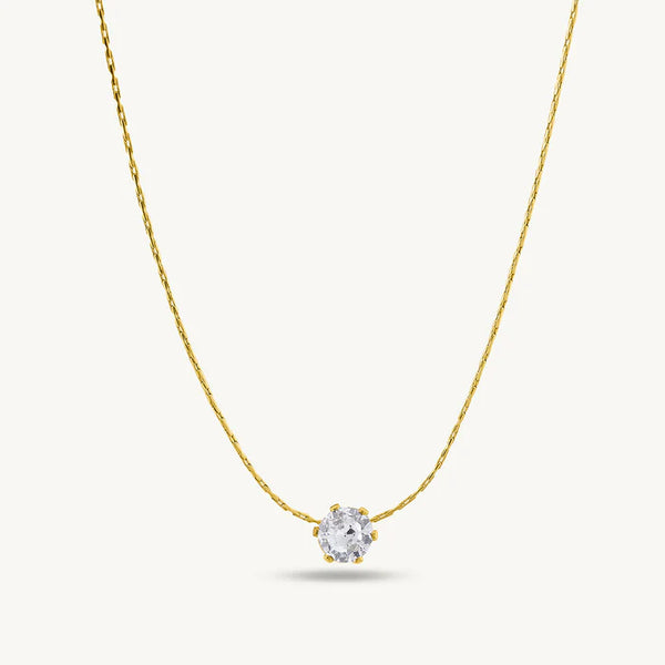 Gold necklace with a clear gemstone pendant on a light gray background