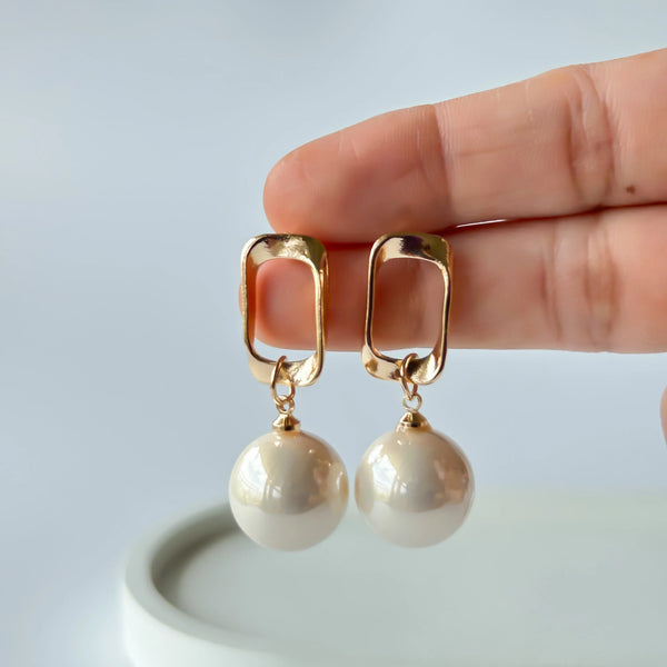 "Close up of gold-toned geometric rectangular earrings with large white pearl drop."