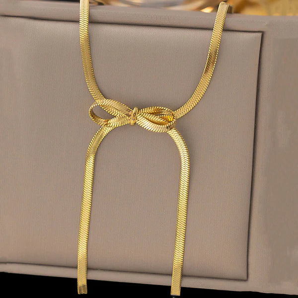 Gold snake chain tied in a bow knot, displayed on a beige background, showcasing the ribbon trend
