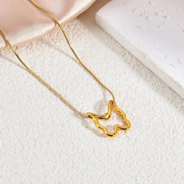 Flat lay of gold abstract butterfly necklace on a snake chain, resting on a textured white surface.