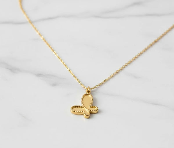 Golden butterfly pendant necklace on a white marble background, minimalist Korean fashion jewellery.