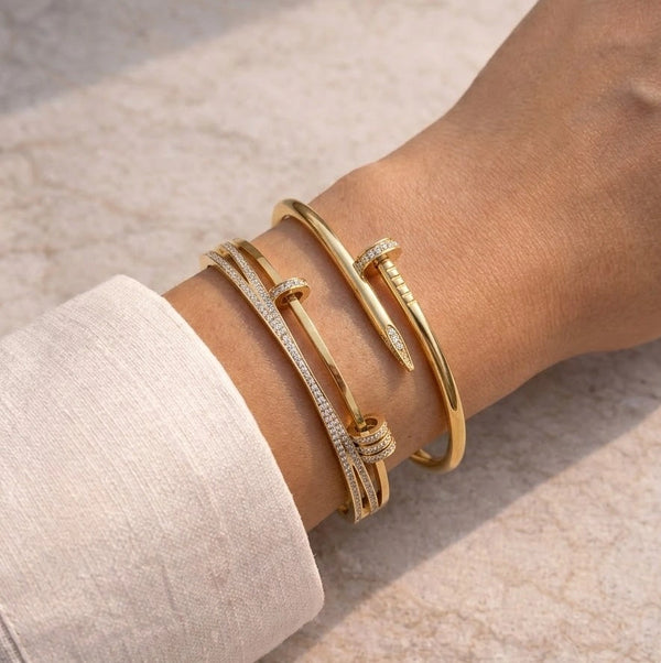 Woman wearing a trendy wrist stack featuring a gold nail bracelet and a layered crystal cuff bangle.