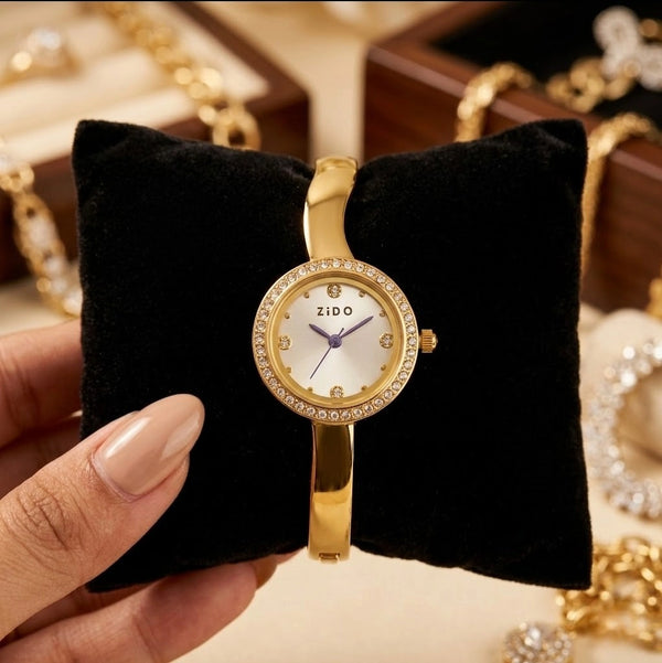 Anti-tarnish gold plated bangle watch with rhinestone bezel resting on a black velvet cushion.