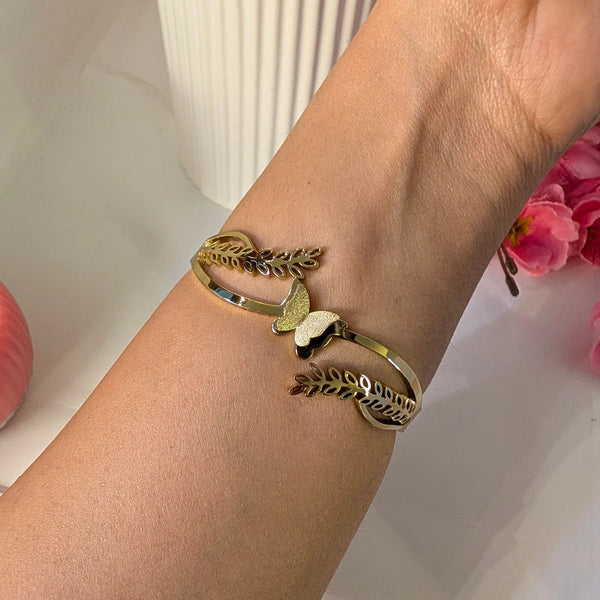 Angled view of gold-plated open cuff bracelet featuring delicate leaf motifs