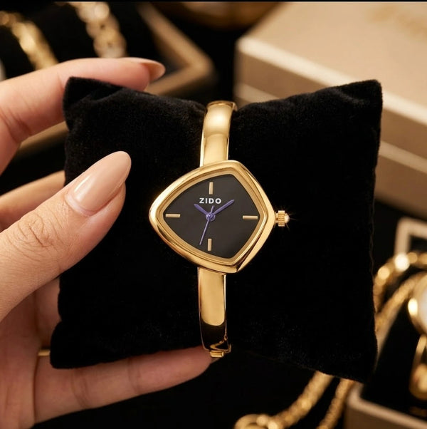 Woman holding a  gold plated anti-tarnish watch with a unique black triangular dial on a velvet cushion.