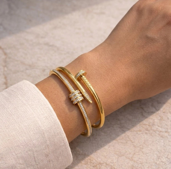 A model's wrist with pink manicure, wearing a stacked set of two gold and diamond-pave bangles: the iconic Juste un Clou nail bracelet and the coiled 'T' design. Showing the full look of the stacked pieces