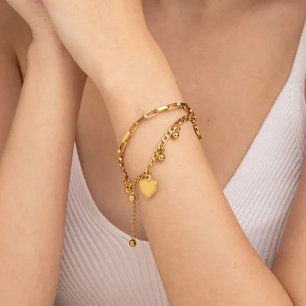 Gold bracelet with heart charm on a person's wrist against a neutral background
