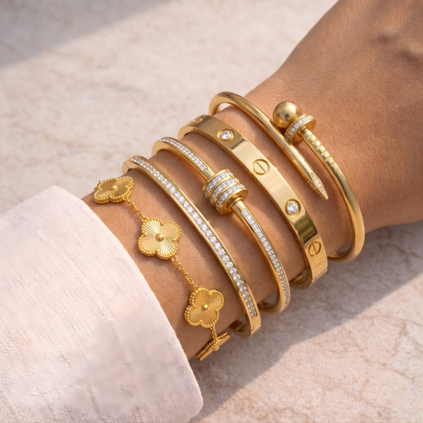 Woman wearing a stylish 5-piece anti-tarnish gold-plated bracelet stack including clover and nail bangles in natural sunlight.
