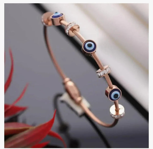 Korean style minimal evil eye charm bracelet in rose gold plating next to a glass decor piece