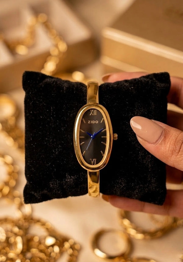 Close up of a Moncheri oval dial anti-tarnish gold plated watch worn on a wrist.