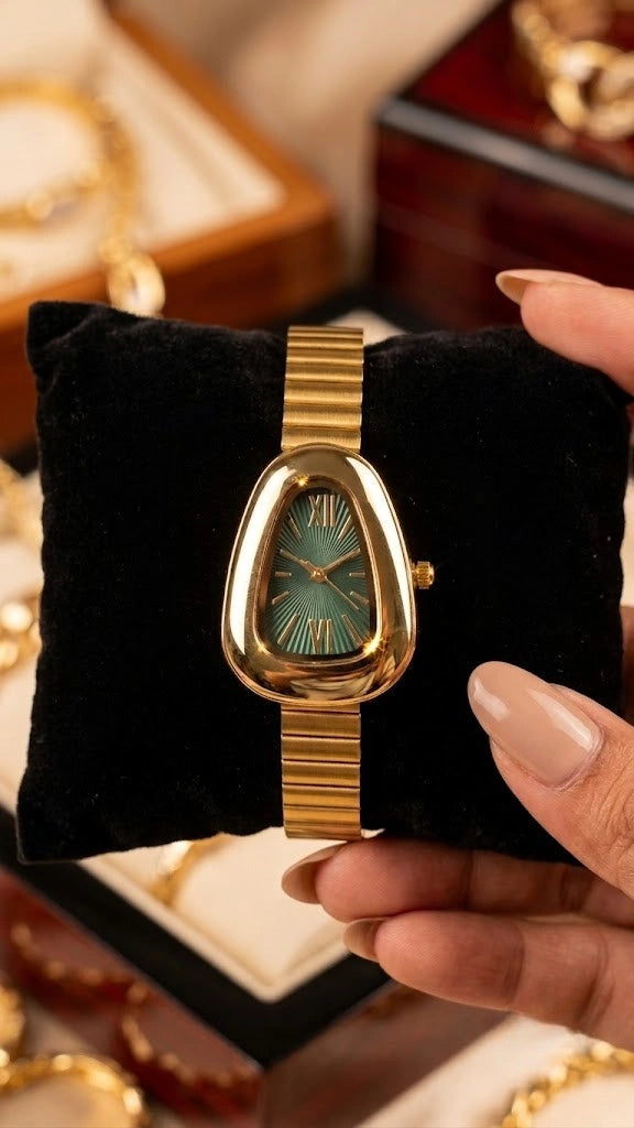MonCheri vintage teardrop emerald green dial watch in anti-tarnish gold plating resting on a black display cushion.