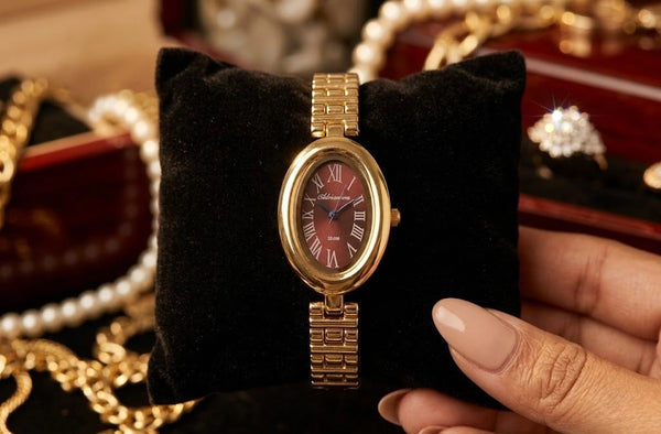 Front angle of an elegant oval-shaped watch featuring a deep maroon dial and an anti-tarnish gold plated metallic link strap.