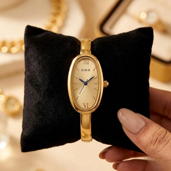 Vintage style oval gold plated watch for women resting on a sleek black velvet cushion.