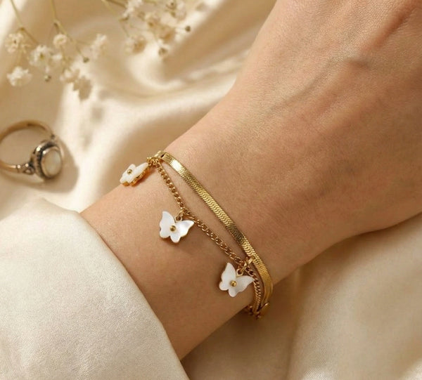Close up details of white enamel flower charms and herringbone chain on gold plated bracelet